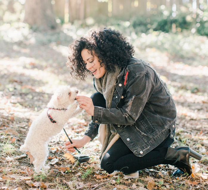 Woman kneeling down to give her small white dog a treat.